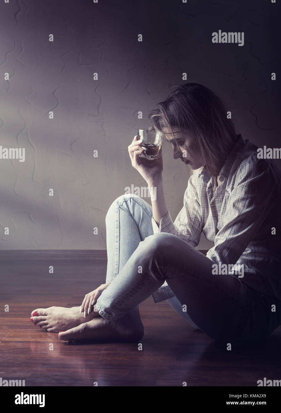 Young woman in depression drinks alcohol while sitting on the floor Stock Photo