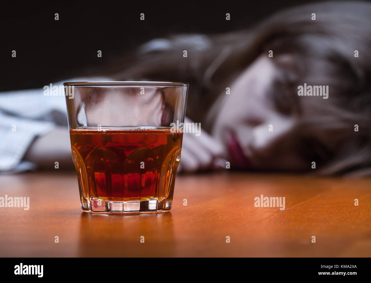 Young woman in depression, drinking alcohol on dark background. Focus on the glass Stock Photo