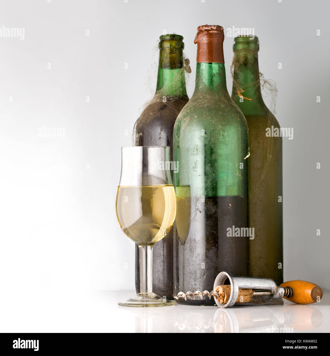 three old bottles of wine, a glass and a corkscrew on a light