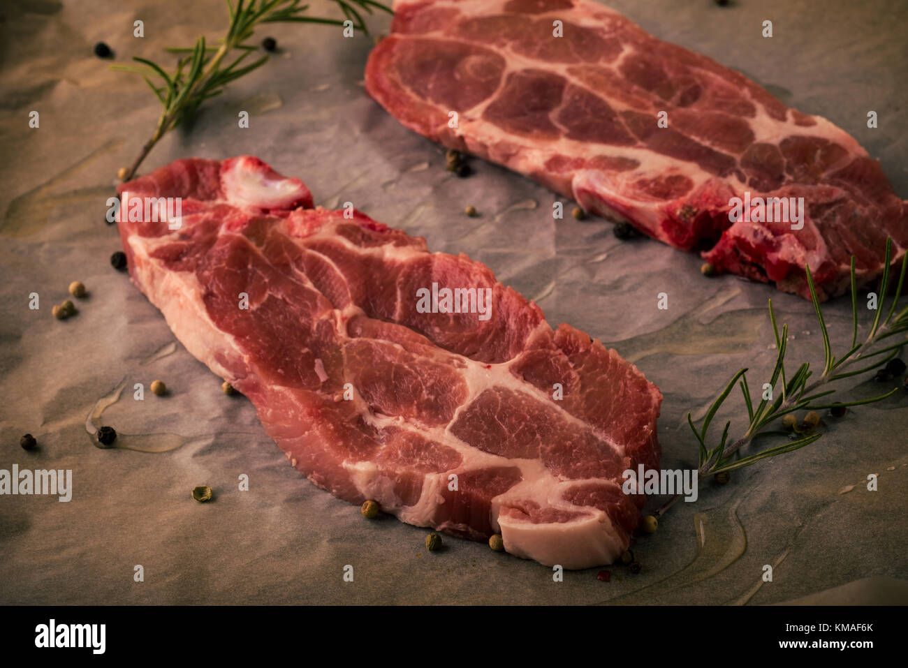 Horizontal photo of two slices of pork neck steaks. The meat portions with red color and fat is placed on worn baking sheet of paper with pepper, rose Stock Photo