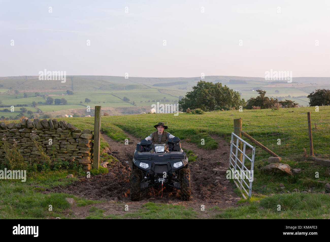A young boy riding a quad on farm land coming through a farm gate on an
