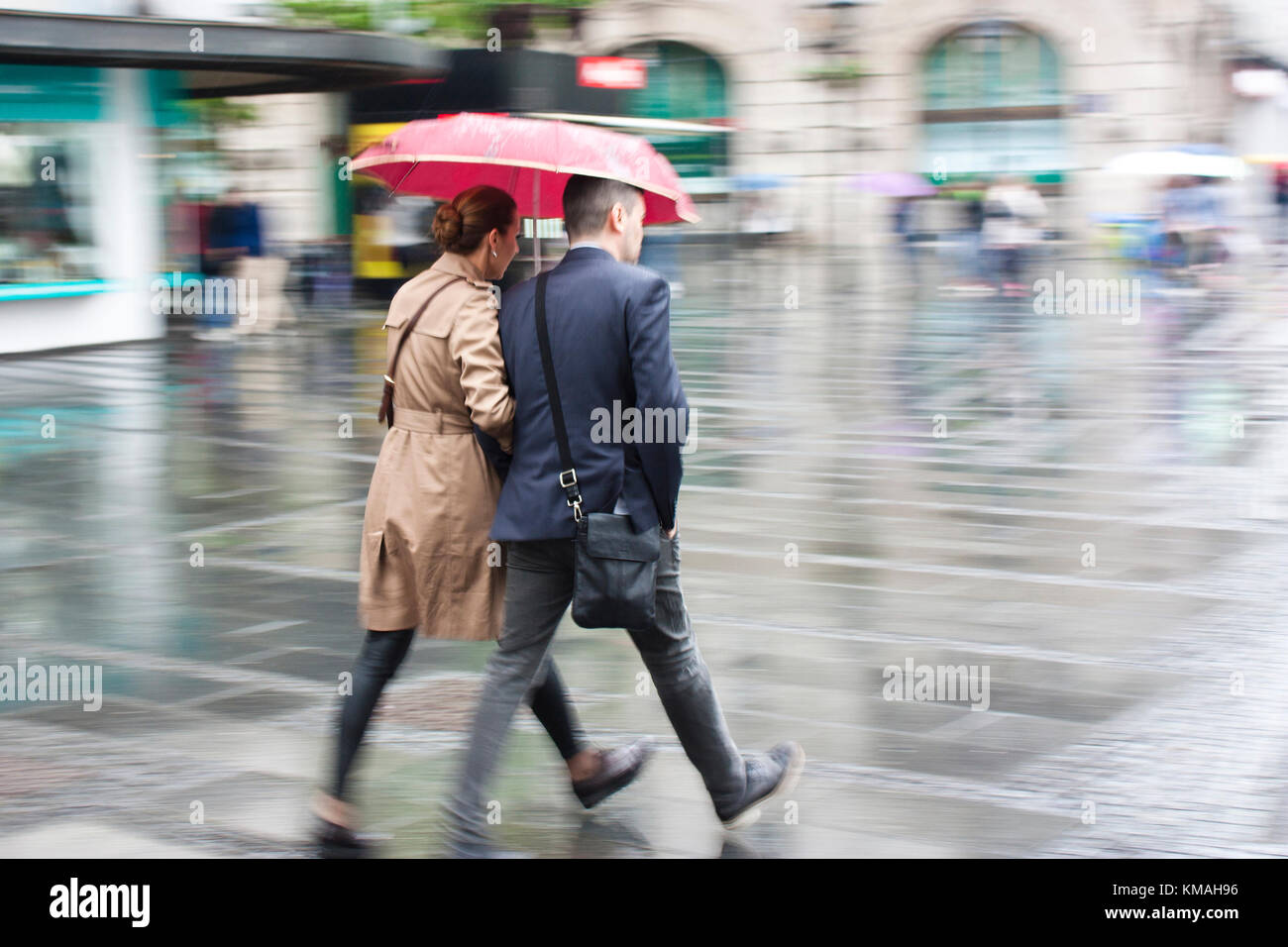 Belgrade, Serbia- May 5, 2017: Young man and woman walking in a hurry under umbrella on rainy and blurry city street Stock Photo