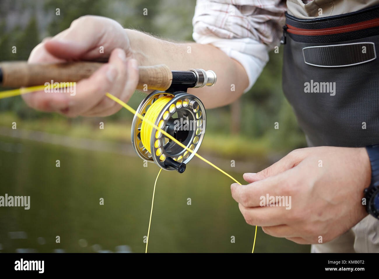 Fly fisherman using a spinning reel with yellow line in a close up view on  his hands against water with green reflections Stock Photo - Alamy