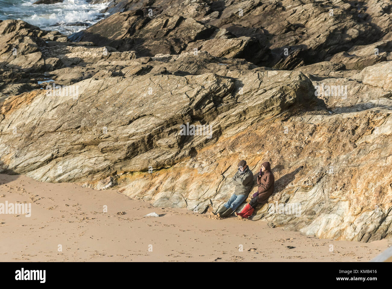 Two people couple sitting on rocks and enjoying the late evening sunshine on Fistral Beach Newquay Cornwall UK. Stock Photo
