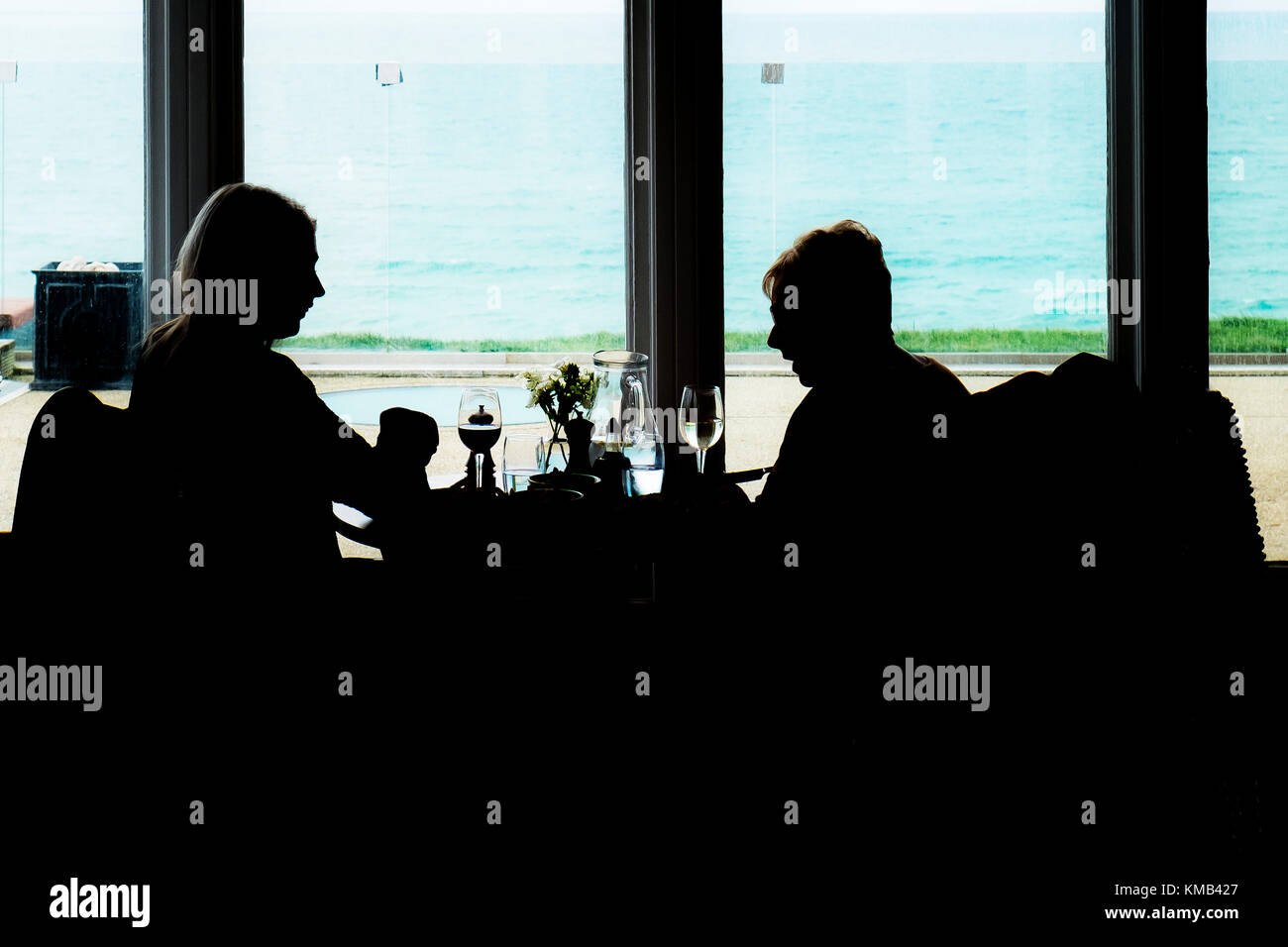 Two women seen in silhouette sitting next to a window in a restaurant. Stock Photo