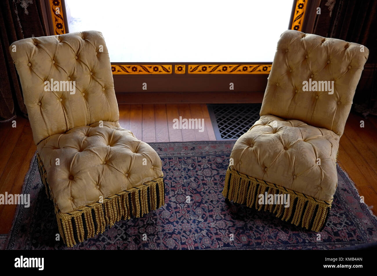 A pair of chairs framed by a window made by placing a filigree pattern cut out of black paper between sheets of plain and amber glass Stock Photo