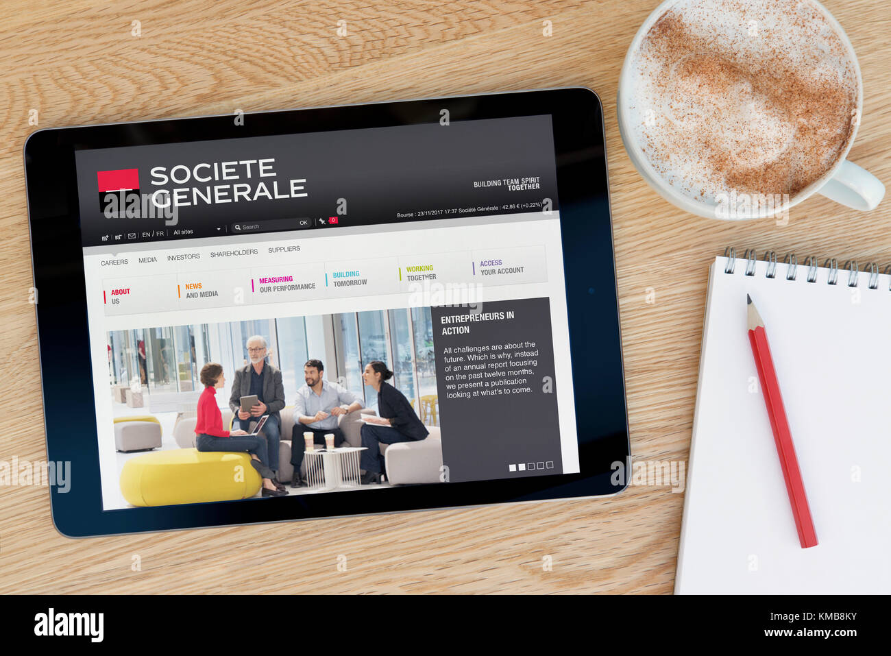 The Societe Generale website features on an iPad tablet device which rests on a wooden table beside a notepad and pencil and a cup of coffee (Editoria Stock Photo