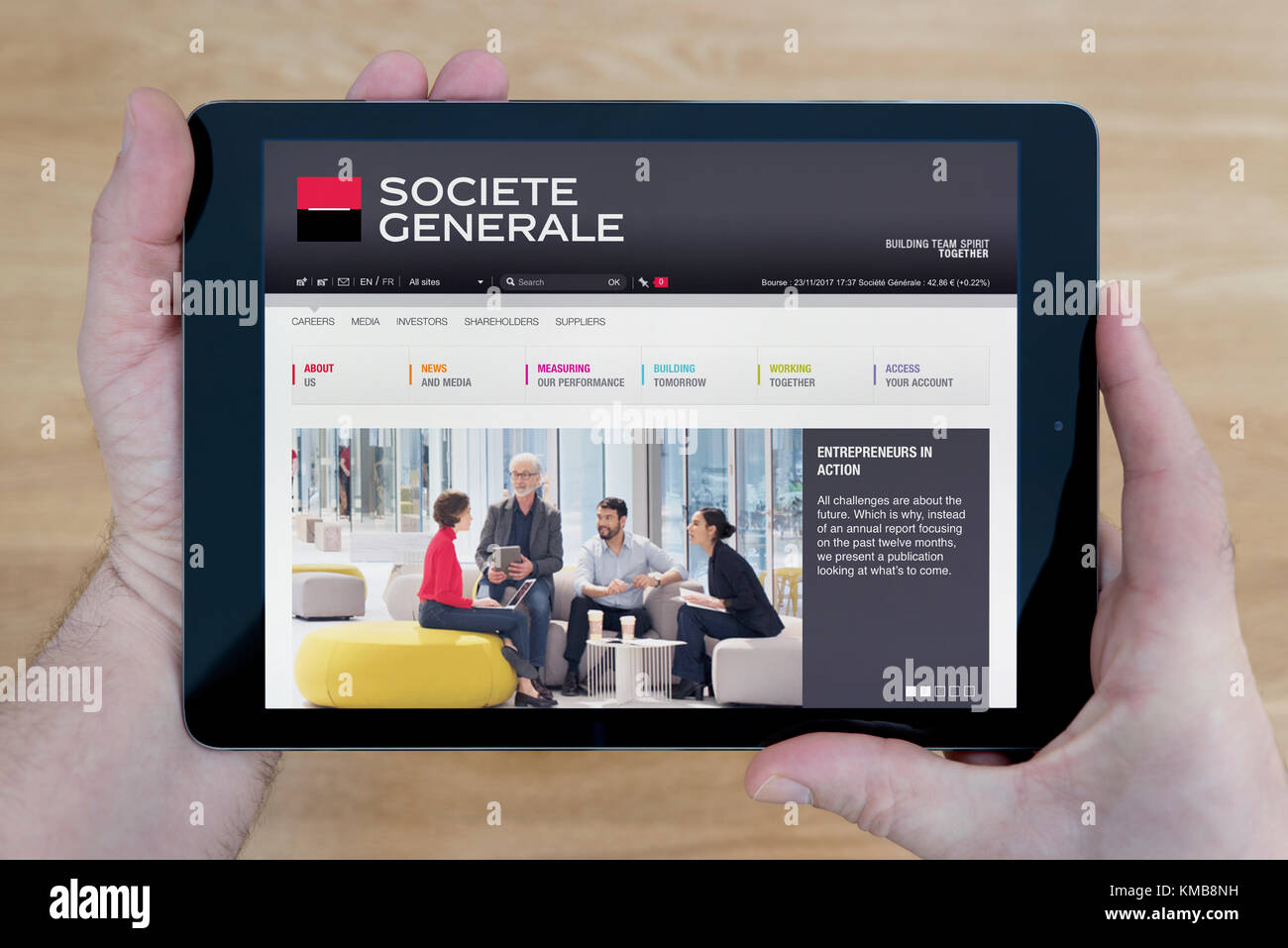A man looks at the Société Générale website on his iPad tablet device, shot against a wooden table top background (Editorial use only) Stock Photo