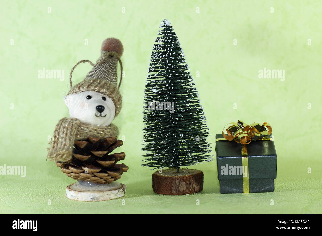 a small gift and a toy bear with a hat next to a decorative chrismas tree on a green background Stock Photo