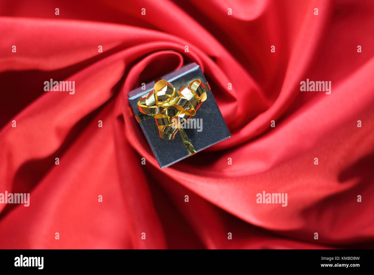 a gift with ribbon placed in the center of a spiral of red satin fabric Stock Photo