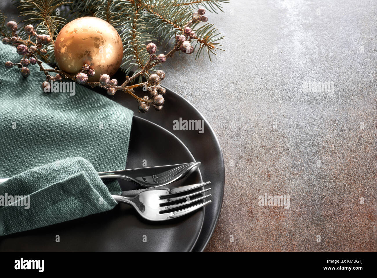 Christmas menu concept with black plates and cutlery decorated with Christmas tree twig and ribbons on rustic background, in turquoise and brown, text Stock Photo