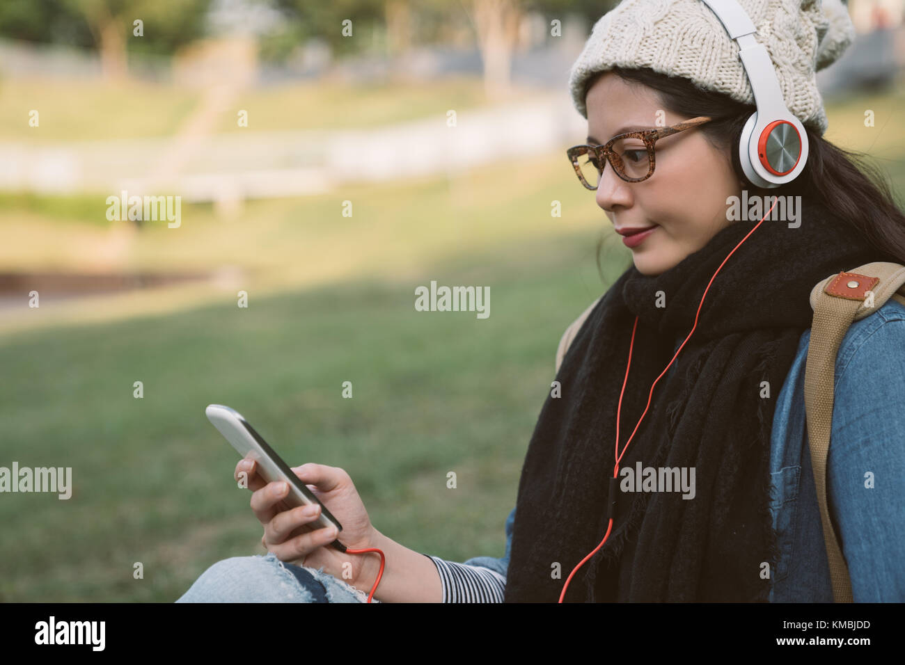 casual beauty girl listening to the music with the smartphone in the winter park on a sunny day. Stock Photo