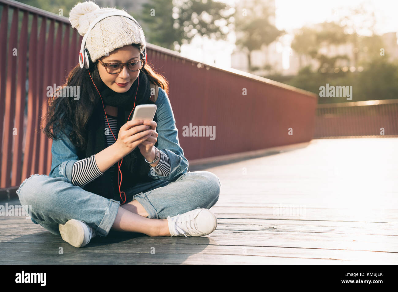 Young stylish pretty woman using smartphone app on city bridge, girl enjoy sunny day in the winter season. Stock Photo