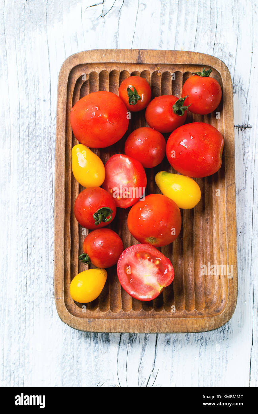 Wooden plate with mix of red and yellow cherry tomatoes over white wooden table. See series. Top view. Stock Photo