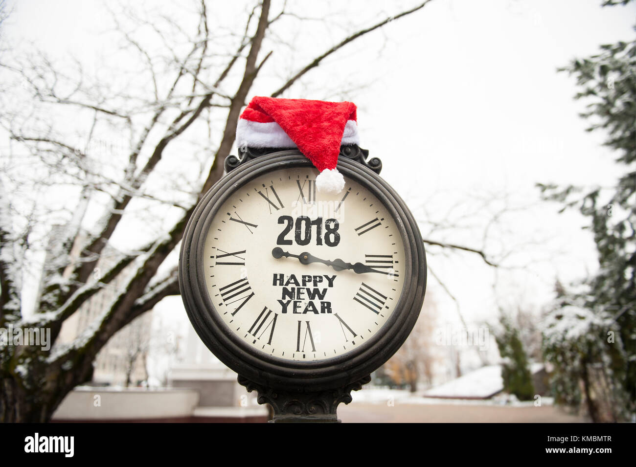 vintage old street clock with the inscription Happy New Year 2018 and Santa Claus hat on them outdoors in winter park Stock Photo