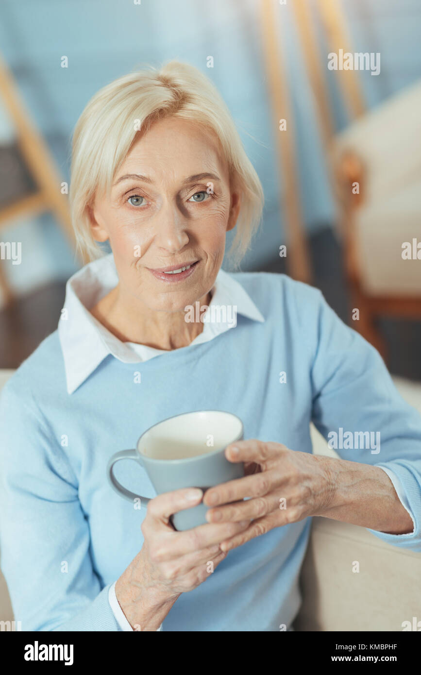 Aged woman feeling satisfied with her tasty tea while sitting at home Stock Photo