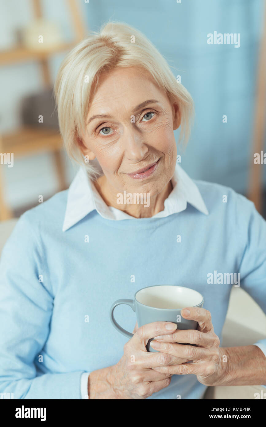 Pleasant senior lady feeling calm while drinking hot tea Stock Photo