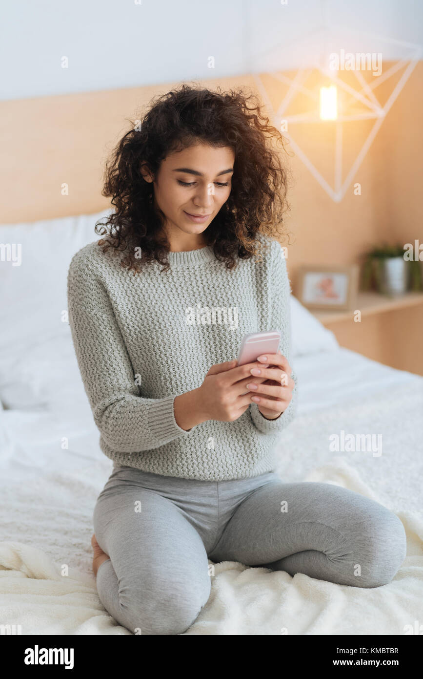 Beautiful girl using smartphone while sitting on bed Stock Photo - Alamy