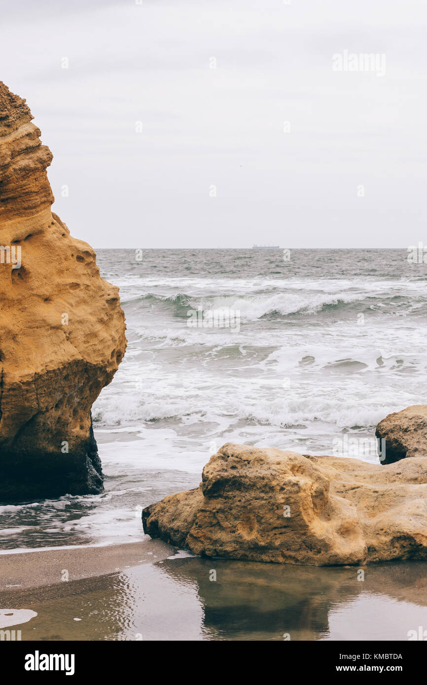 View of the rocks and the sea from the beach in cloudy weather ...