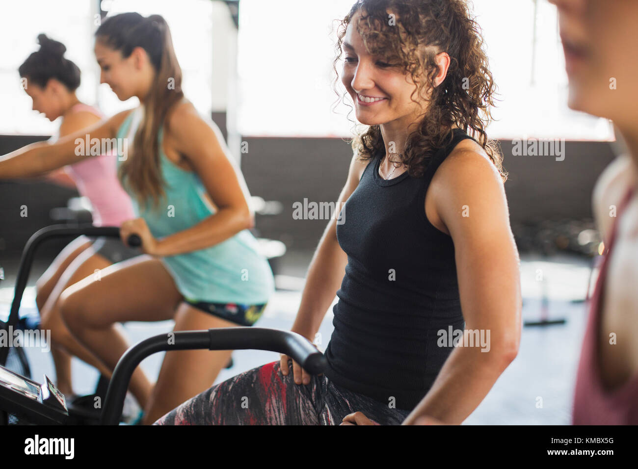 Smiling young woman riding elliptical bike in exercise class Stock Photo