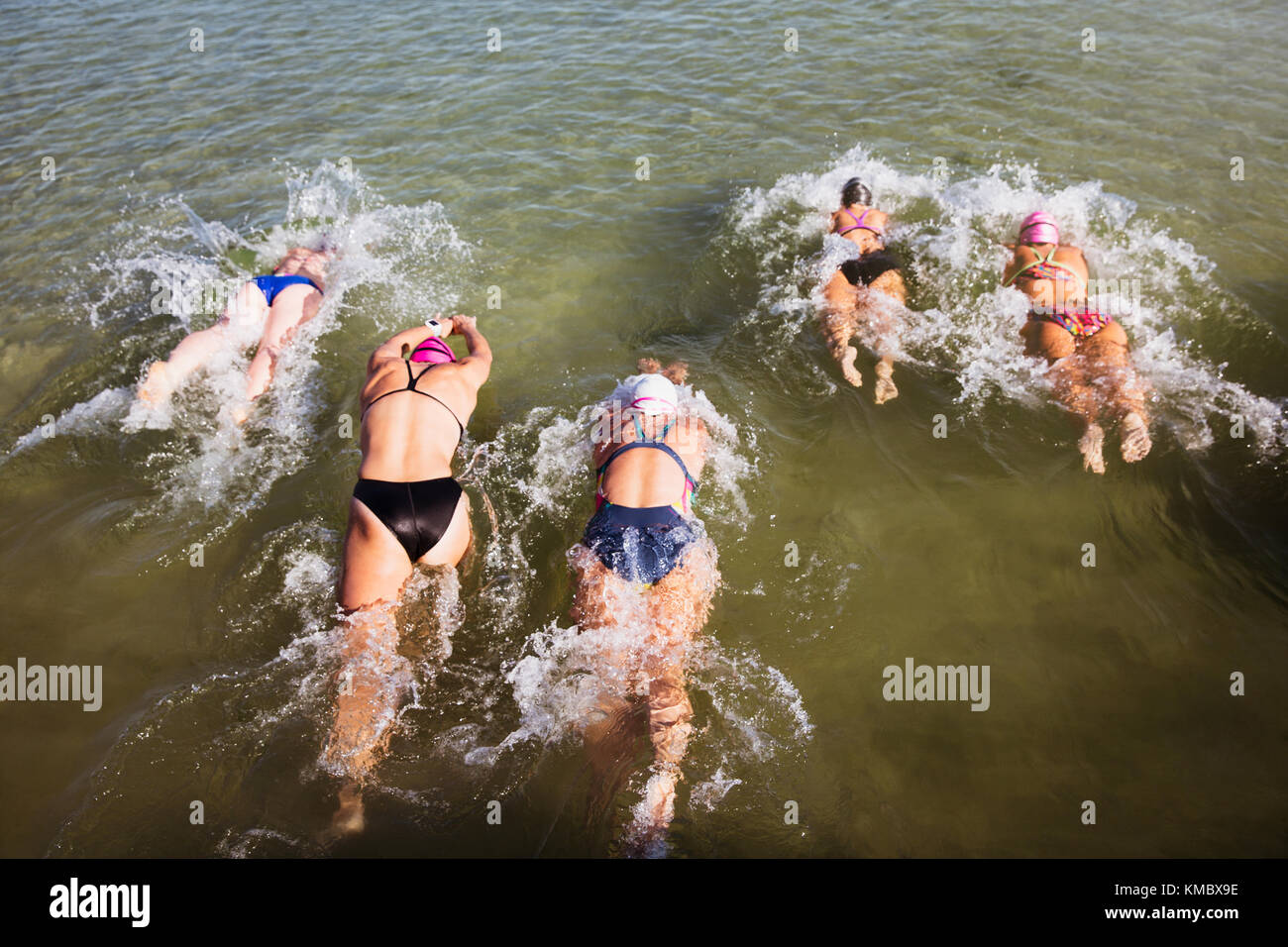Overhead view female open water swimmers swimming in sunny ocean Stock Photo