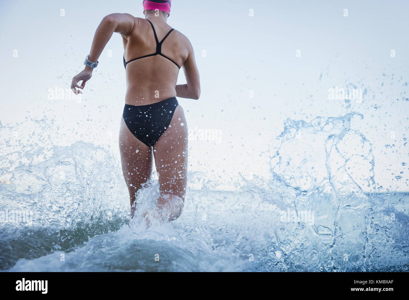 Female open water swimmers running and splashing in ocean surf Stock Photo