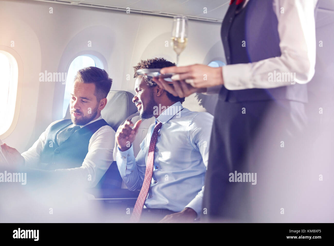 Flight attendant serving champagne to businessmen in first class on airplane Stock Photo
