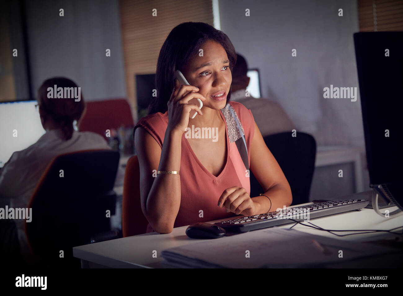 Businesswoman working late,talking on smart phone at computer in dark office Stock Photo