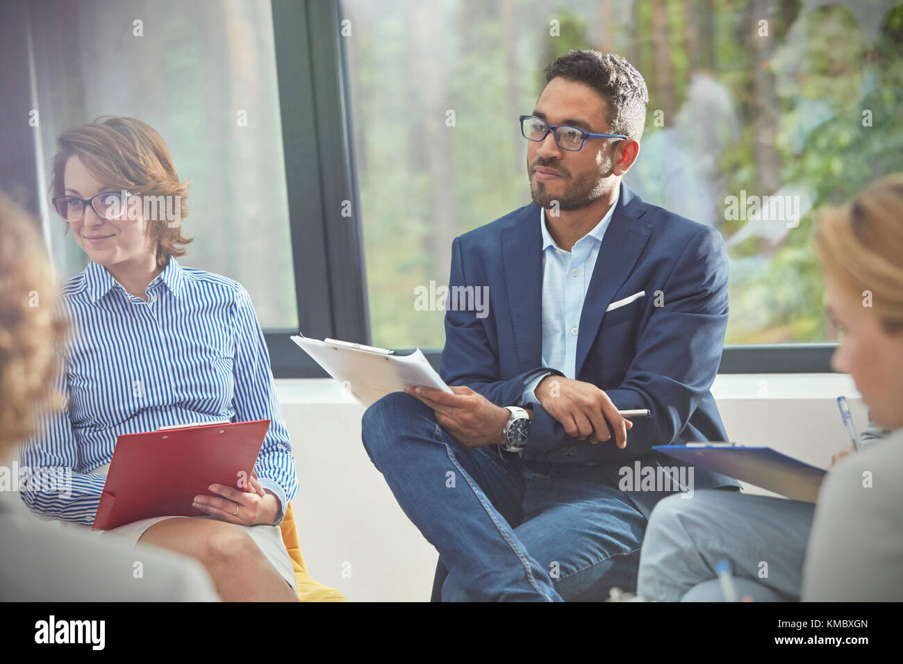 Attentive man with clipboard listening in group therapy session Stock Photo