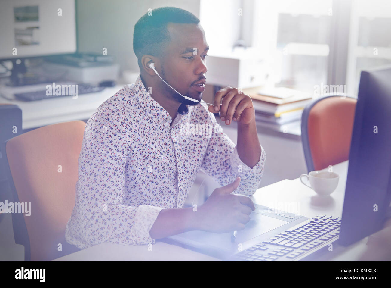 Male graphic designer working at computer in graphics tablet,talking on telephone with headphones Stock Photo