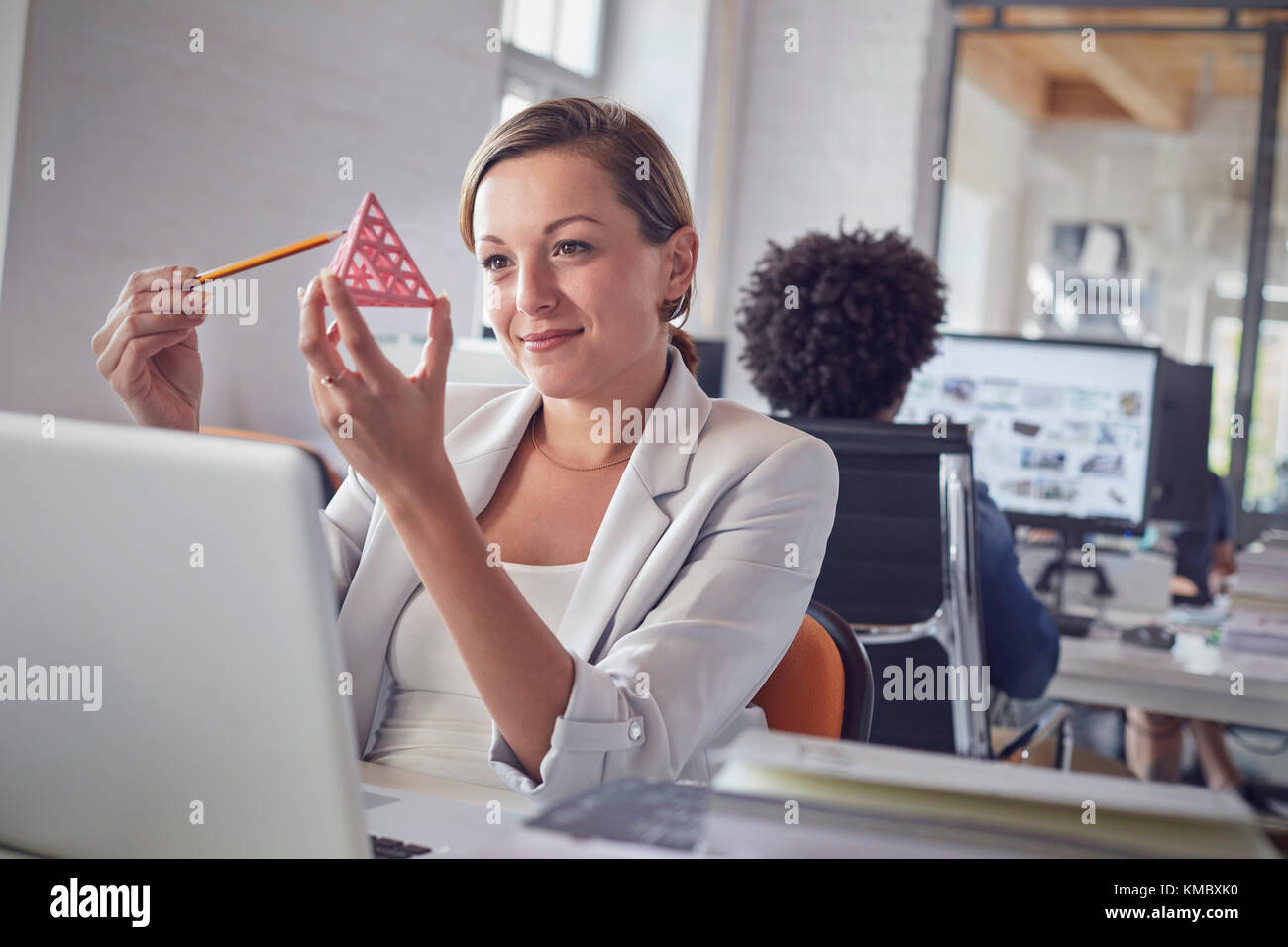 Smiling female design professional examining triangle prototype at laptop in office Stock Photo