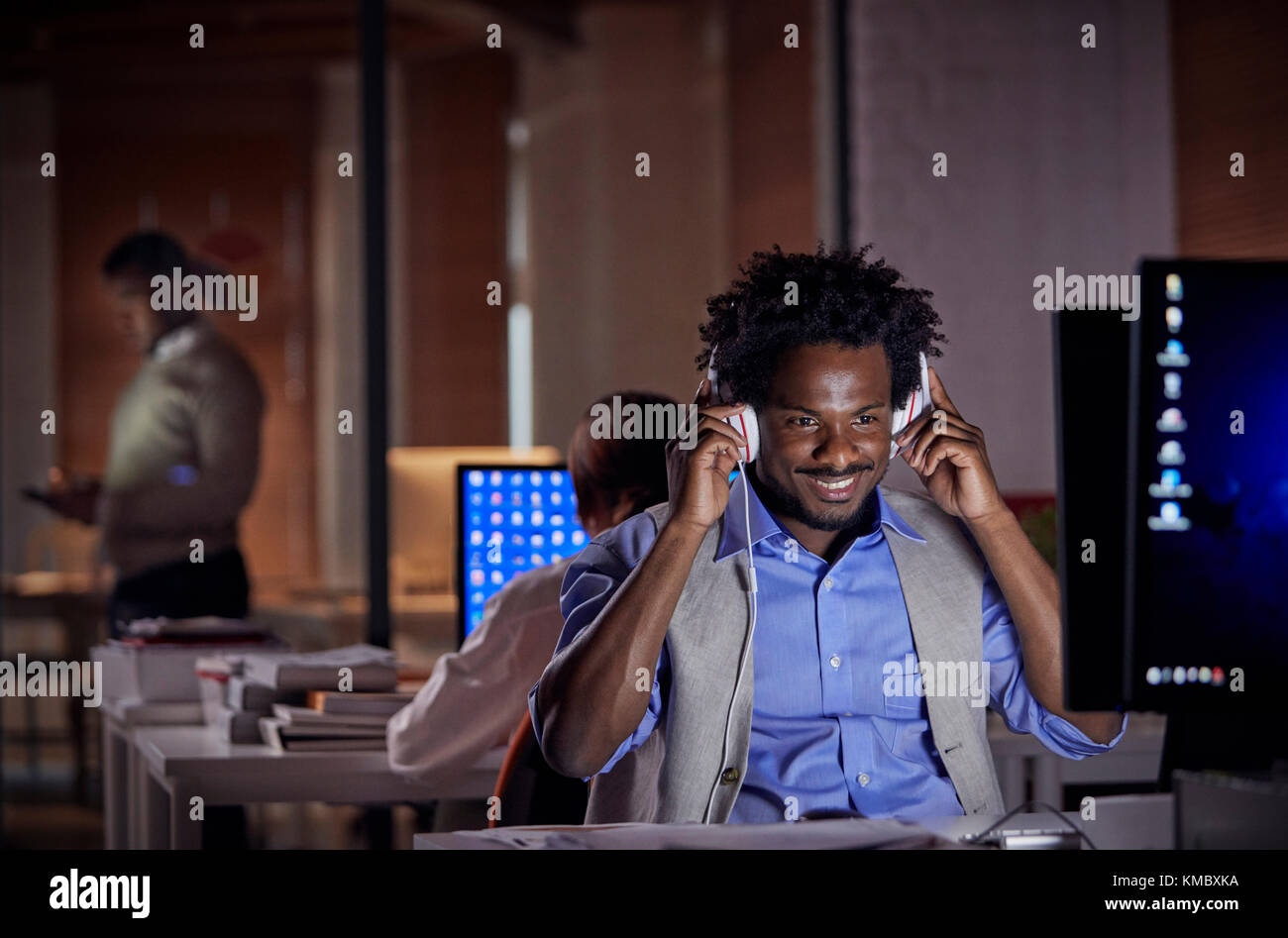 Smiling businessman with headphones listening to music,working late at computer in dark office at night Stock Photo
