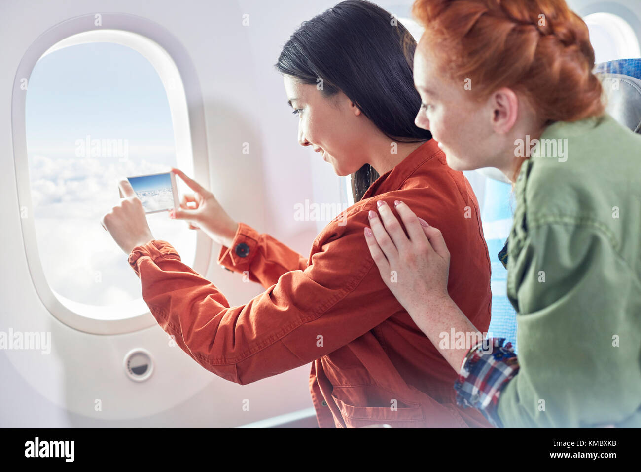 Young women friends using camera phone at airplane window Stock Photo