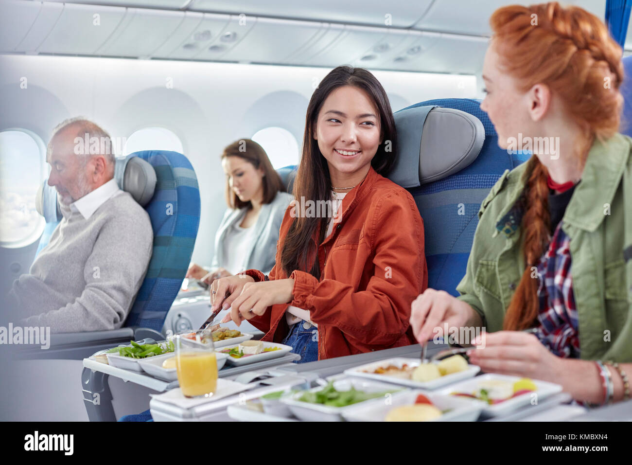 Women friends eating dinner and talking on airplane Stock Photo