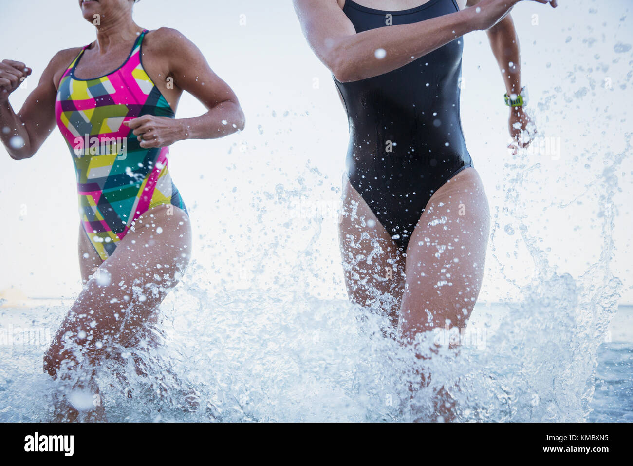 Female open water swimmers running and splashing in ocean surf Stock Photo