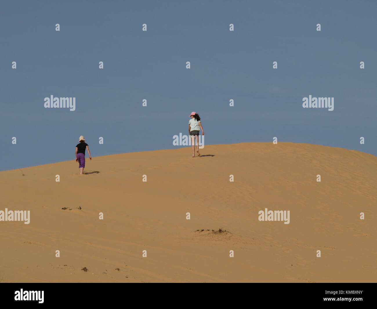 2 girls climbing on a sand dune on the sky background Stock Photo