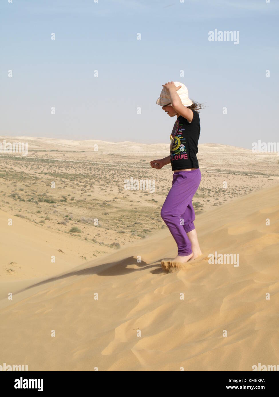 girl standing on sand dune and holding her hat from from the wind in the desert Stock Photo