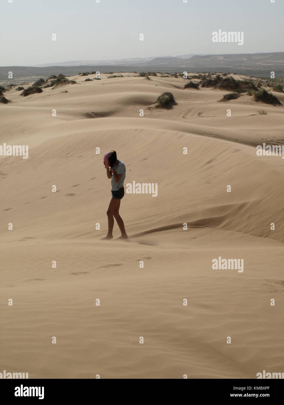 girl standing on sand dune and covering her face from sand storm in the desert Stock Photo