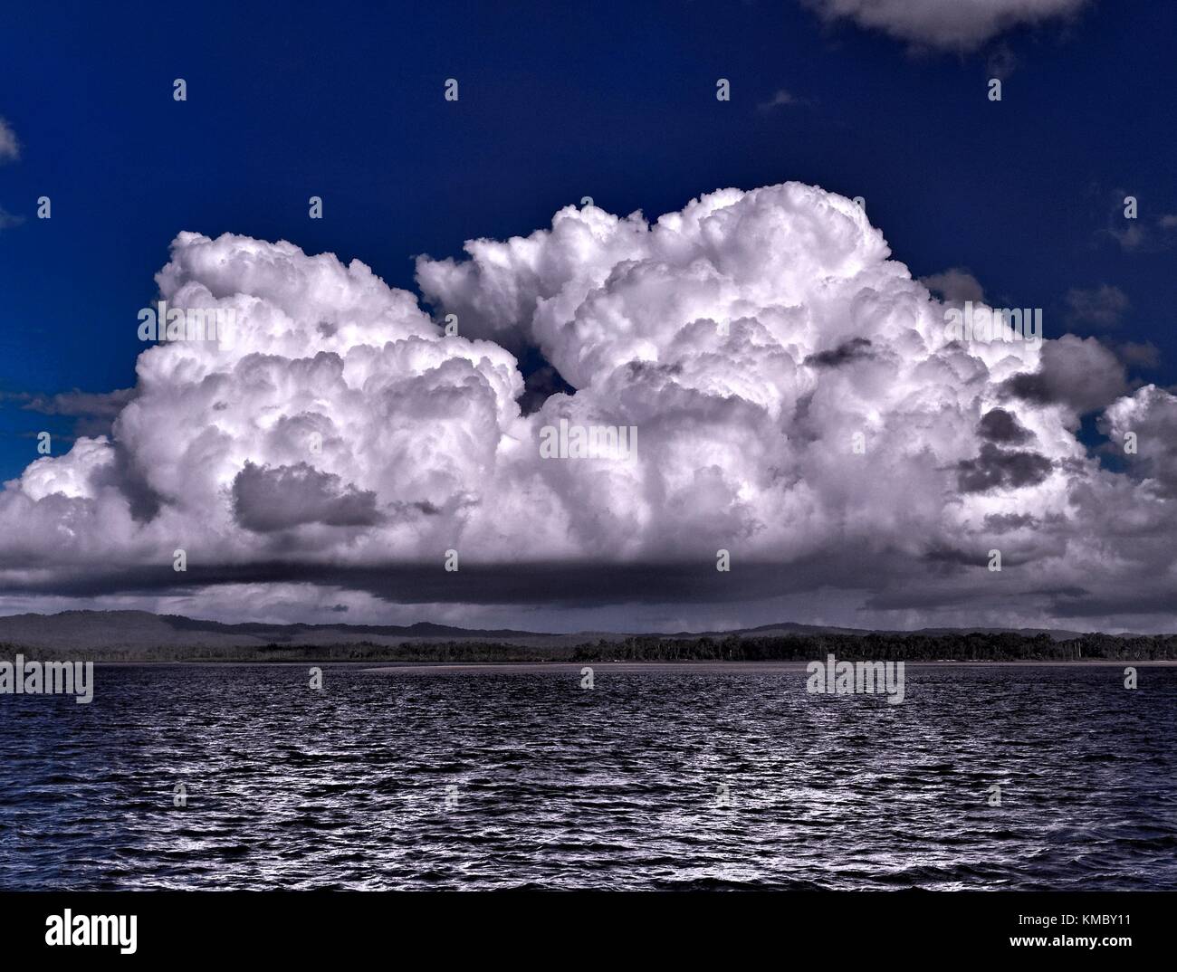 A spectacular dramatic brightly coloured cloudy sea water tropical seascape featuring awesome billowing white Cumulus cloud formation in a  blue sky Stock Photo