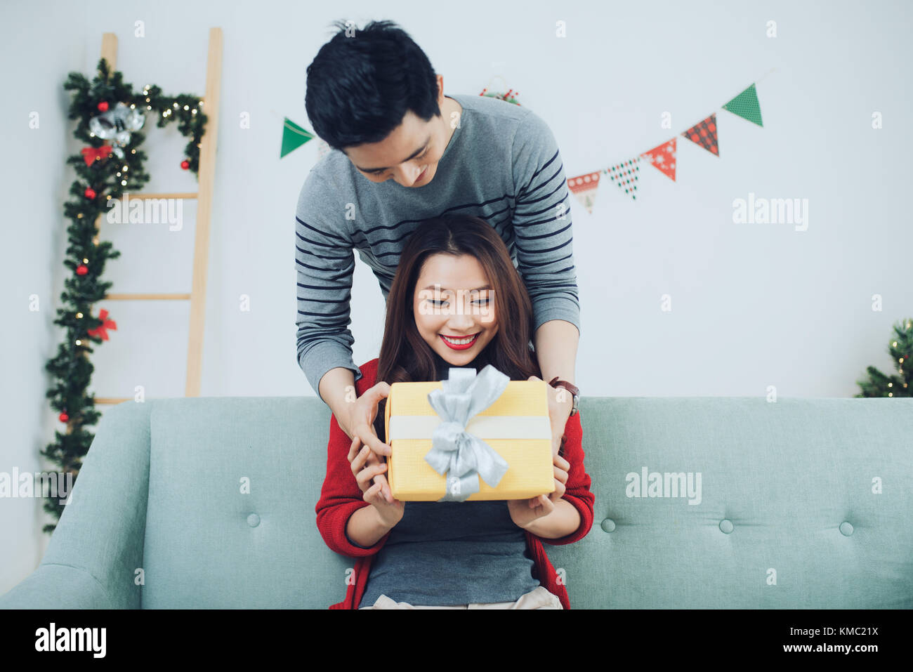 Christmas Asian Couple. A handsome man giving her girlfriend/wife a gift at home celebrating New Year People Stock Photo