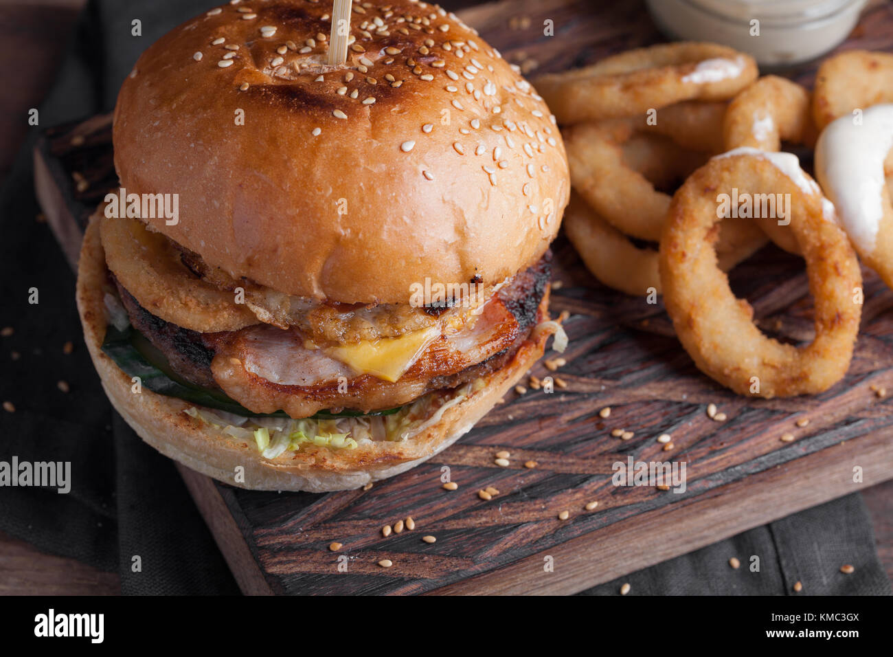 Closeup of a tasty Burger with appetizers such as fried onion rings with a white garlic sauce. Juicy Burger with bacon and cheese on a dark wood backg Stock Photo