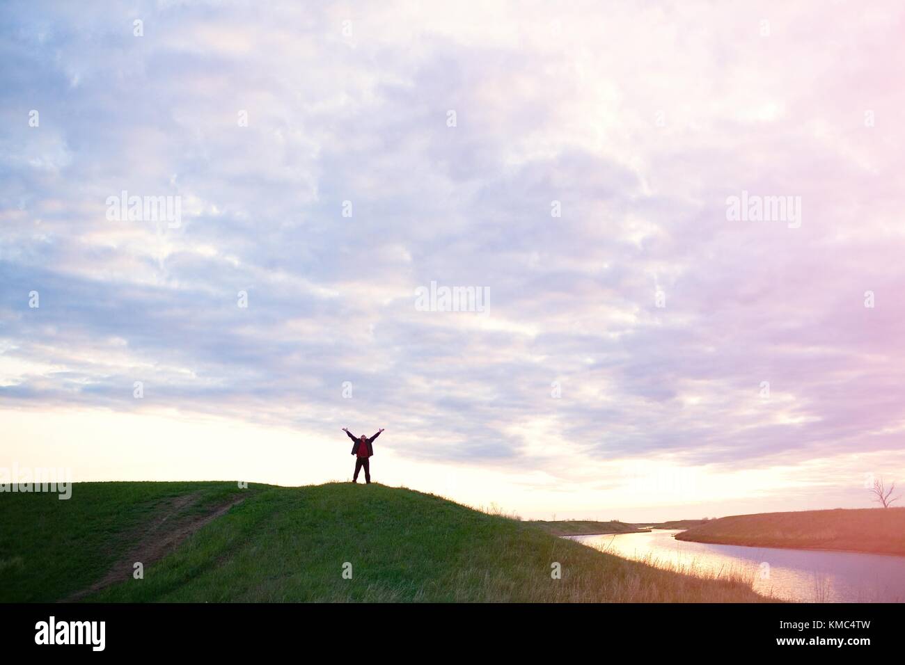 happy man with raised hands by the river on a sunset sky background ...