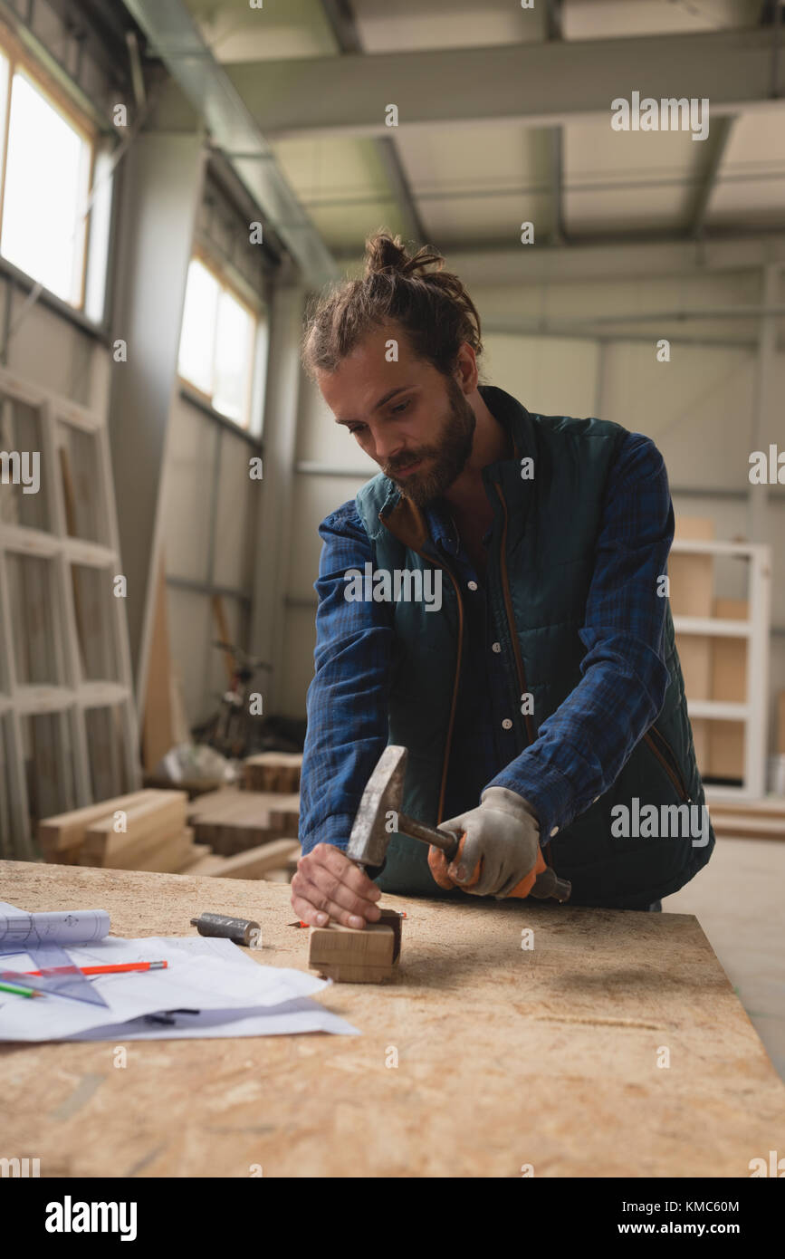 Carpenter making hole in wooden block with hammer Stock Photo