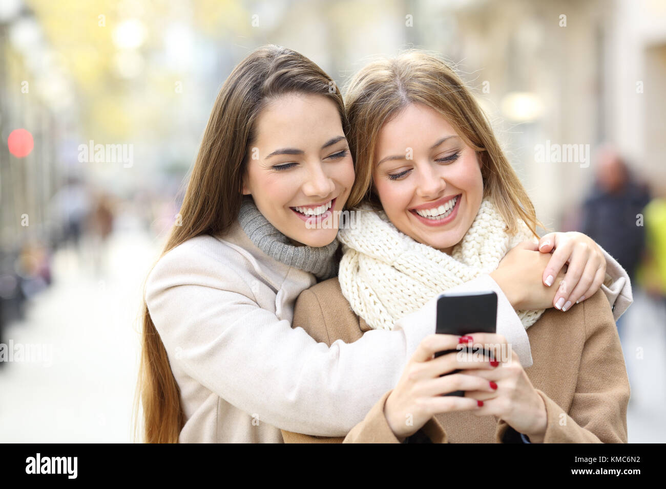 Front view portrait of two cheerful friends watching smart phone content in winter on the street Stock Photo