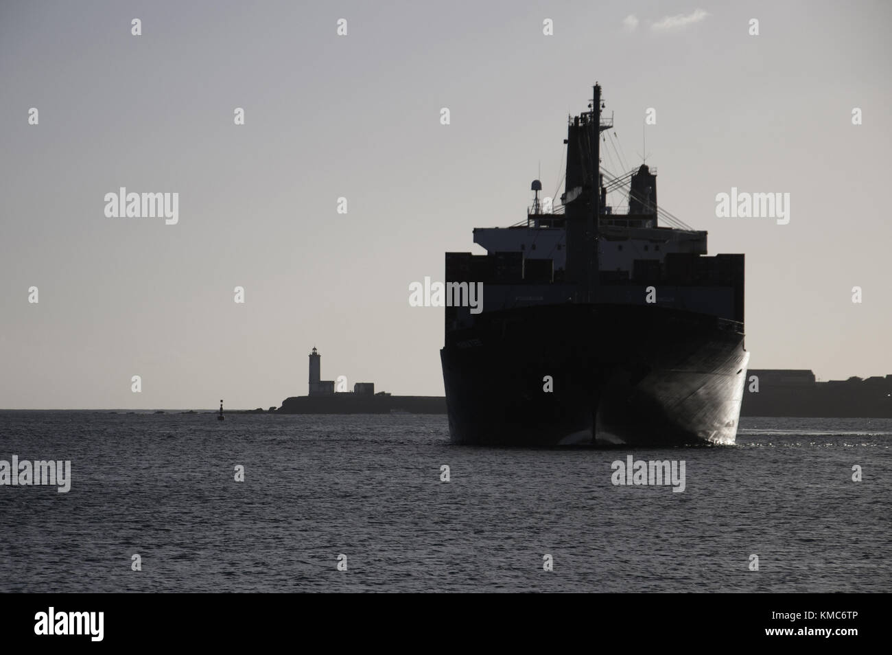 A cargo ship, seeming extra large beside the port lighthouse, entering Praia harbour in Santiago