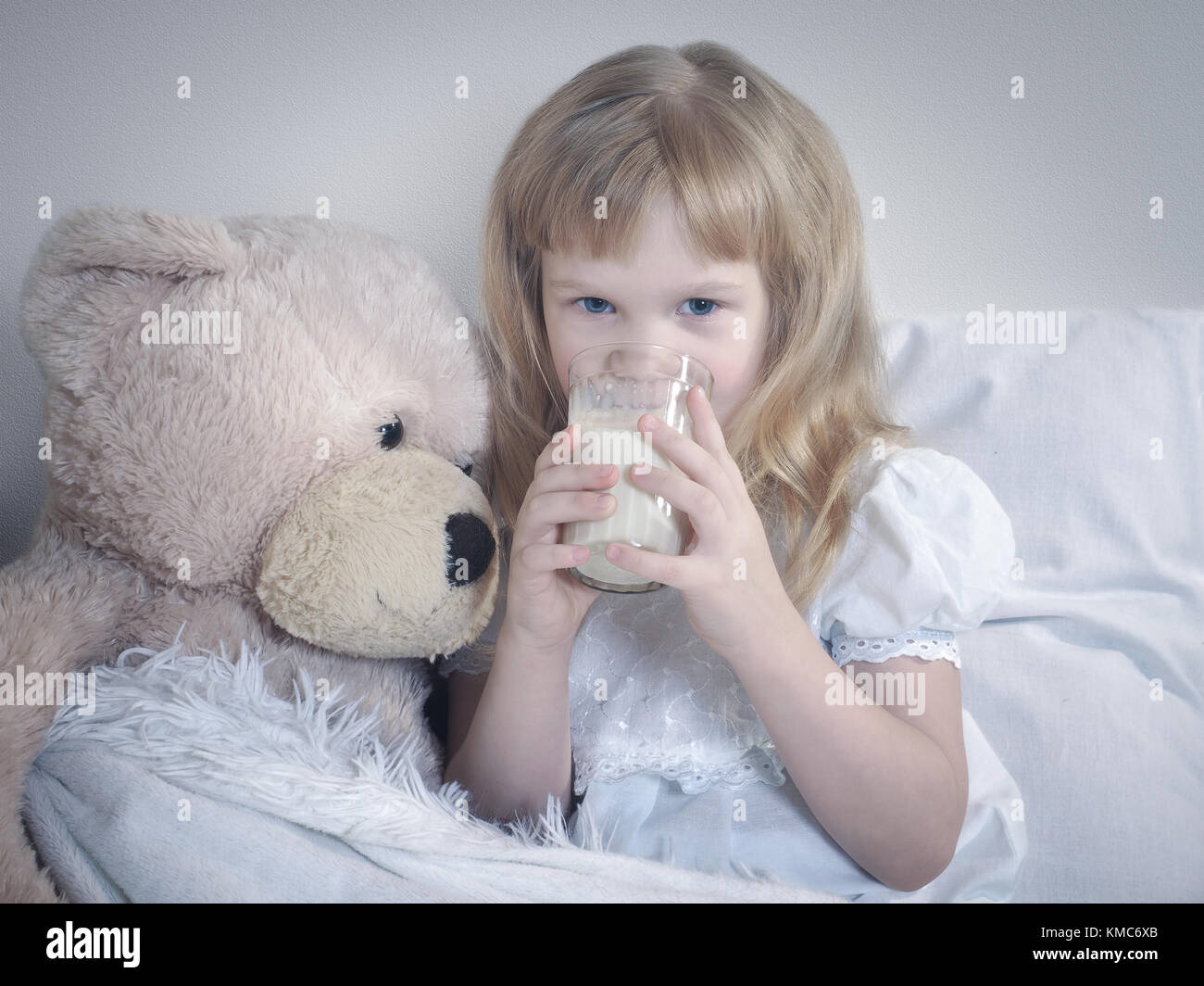 Little girl drinks milk before bedtime. Child in bed with toy big