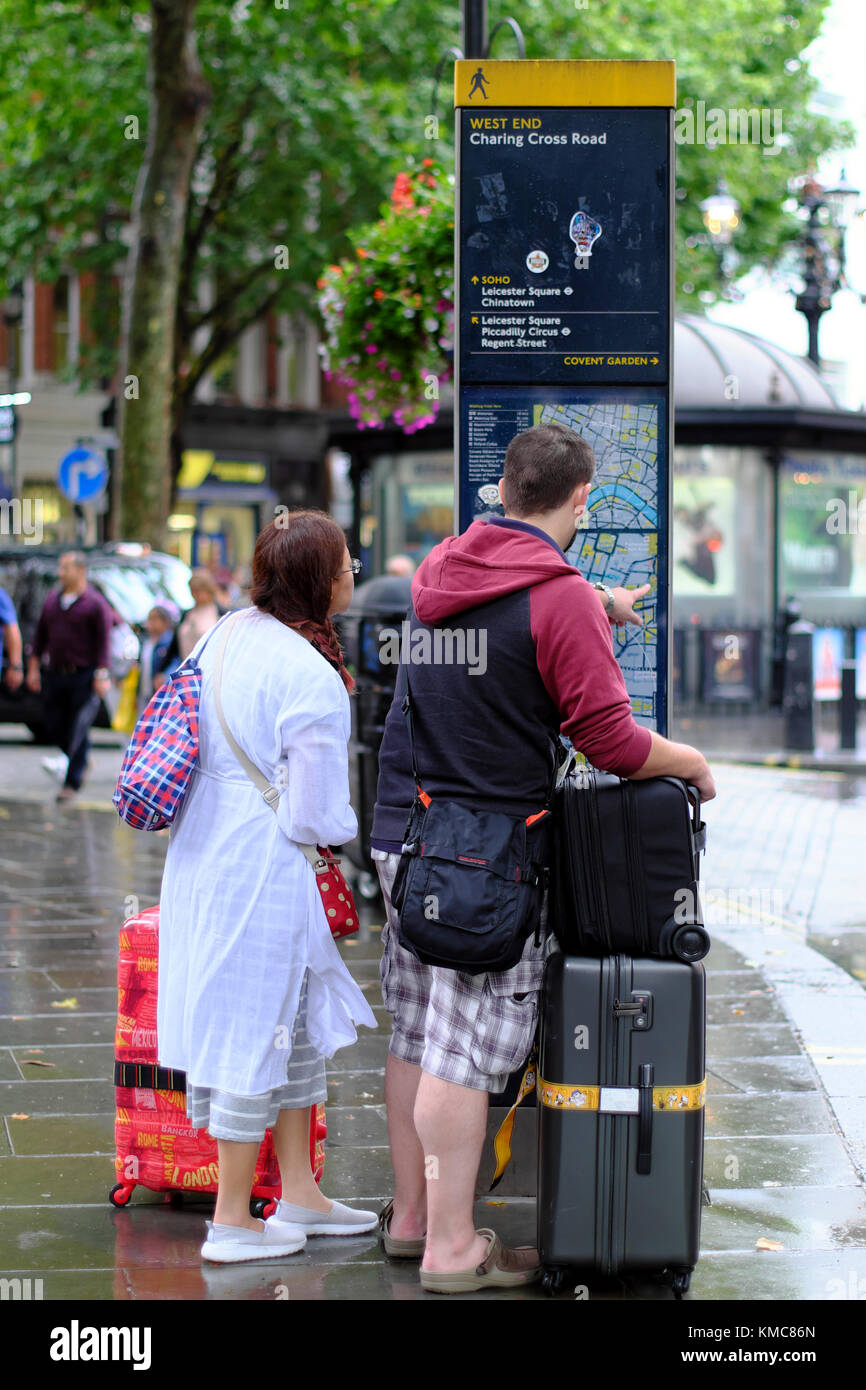 Man and woman with travel luggage looking at map on public information board in the West End, London, England, UK Stock Photo