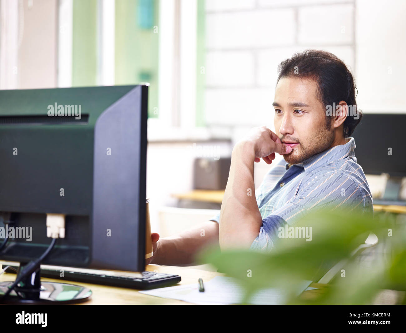 asian businessman in casual wear sitting at desk working in office looking at desktop computer screen. Stock Photo