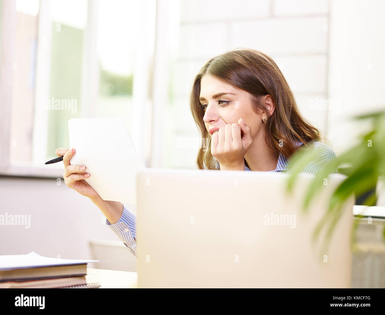 beautiful young caucasian corporate executive businesswoman working in office reading document while using laptop computer. Stock Photo