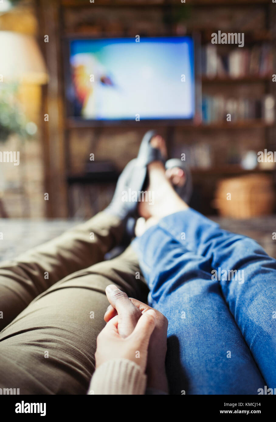 Personal perspective affectionate couple holding hands watching TV in living room Stock Photo